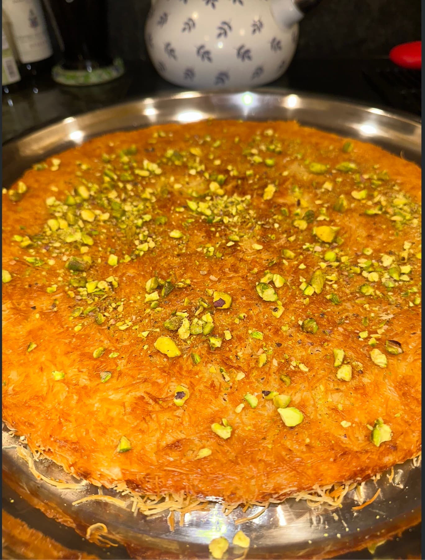 An angled close-up of a knafe tray showing the crisp toasted kataifi crust scattered with pistachios